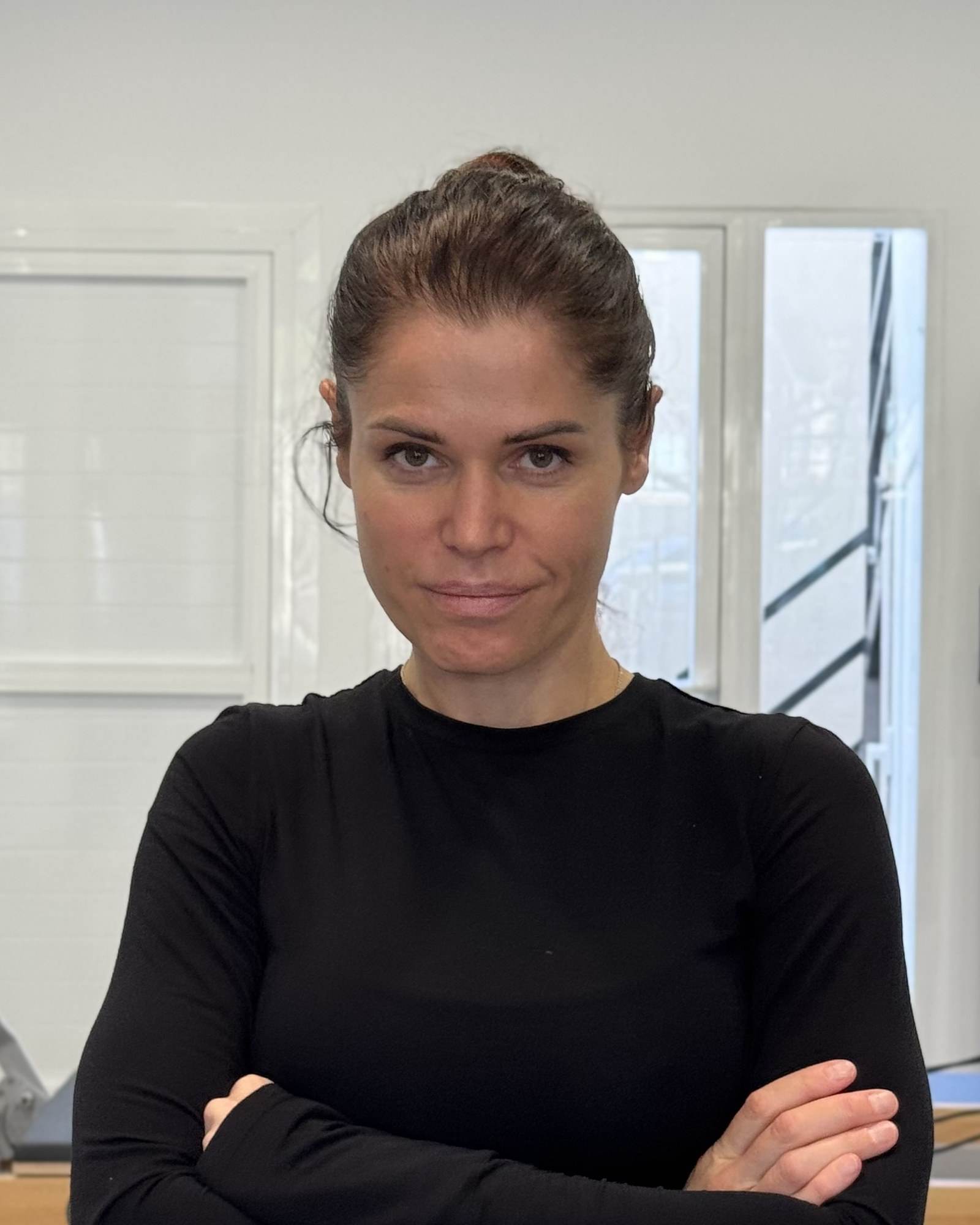 Front-facing portrait of Inna, lead coach, arms crossed in the reformer room